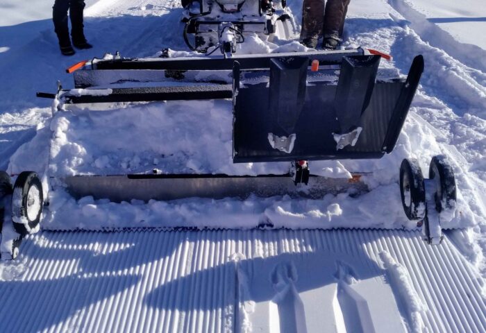 In 2021, Ski Heritage East Head Groomer Lyle Fair (right) works the Ginzu Groomer being towed by a Yahama snowmobile. (The group acquired a second Ginzu in 2022.) Photo supplied by Ski Heritage East