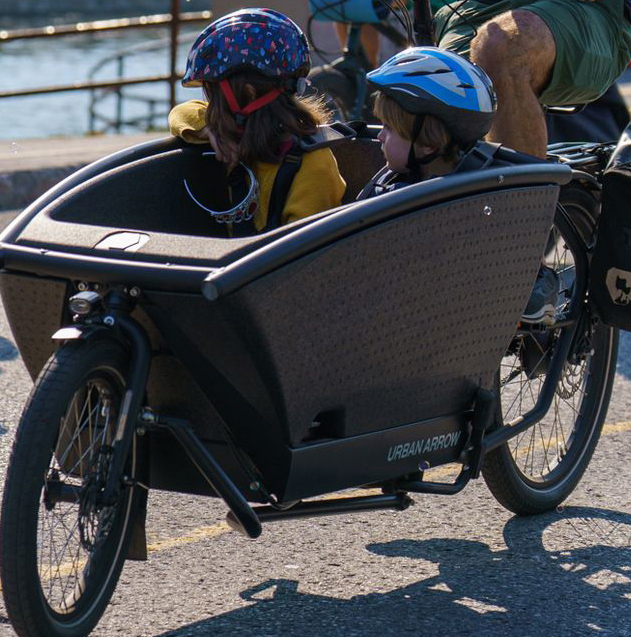 A photo of two children riding in the front trailer of a bike along the canal.