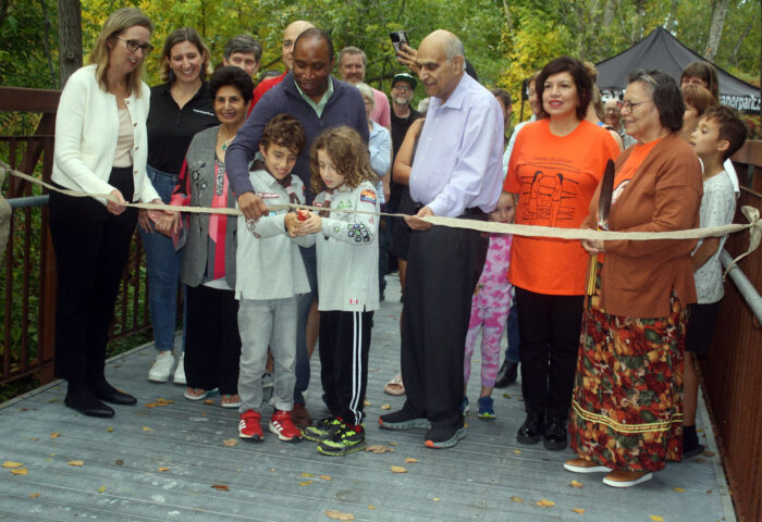 A large group of Manor Park residents and officials gathered Sept. 23 for the inauguration of the Sumac Footbridge, located at the eastern end of Blasdell Avenue. Cutting the ribbon to officially open the structure are Ismael Orion Di Carlo and Michael Acadia Di Carlo, whose father Anthony (standing behind) was a member of the Manor Park Community Council (MPCC) bridge naming committee. Also shown here (left to right) are Émilie Girard-Ruel of the National Capital Commission; Kelsey McMahon of the bridge naming committee; Mrs Saroj Aggarwal; Di Carlo: Rideau-Rockcliffe Councillor Rawlson King; Mr. Anand Aggarwal; Anita Tenasco and her mother Jenny Buckshot Tenasco of Kitigan Zibi. PHOTO: RYLAND COYNE