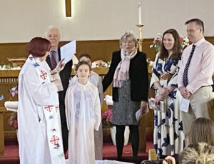 Reverend Susan Lewis (left) prepares to baptize young Beatrice Trudeau (centre front) and her brother Niall (back) during the Easter service. Looking on (left to right) are the children's grandparents Brian and Mary Wolff, and parents Clara and Mike Trudeau. PHOTO: DIANA POITRAS